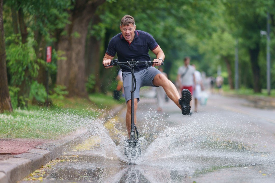 Un hombre atraviesa un gran charco en patinete eléctrico y el agua salpica – circular con lluvia y grado IP