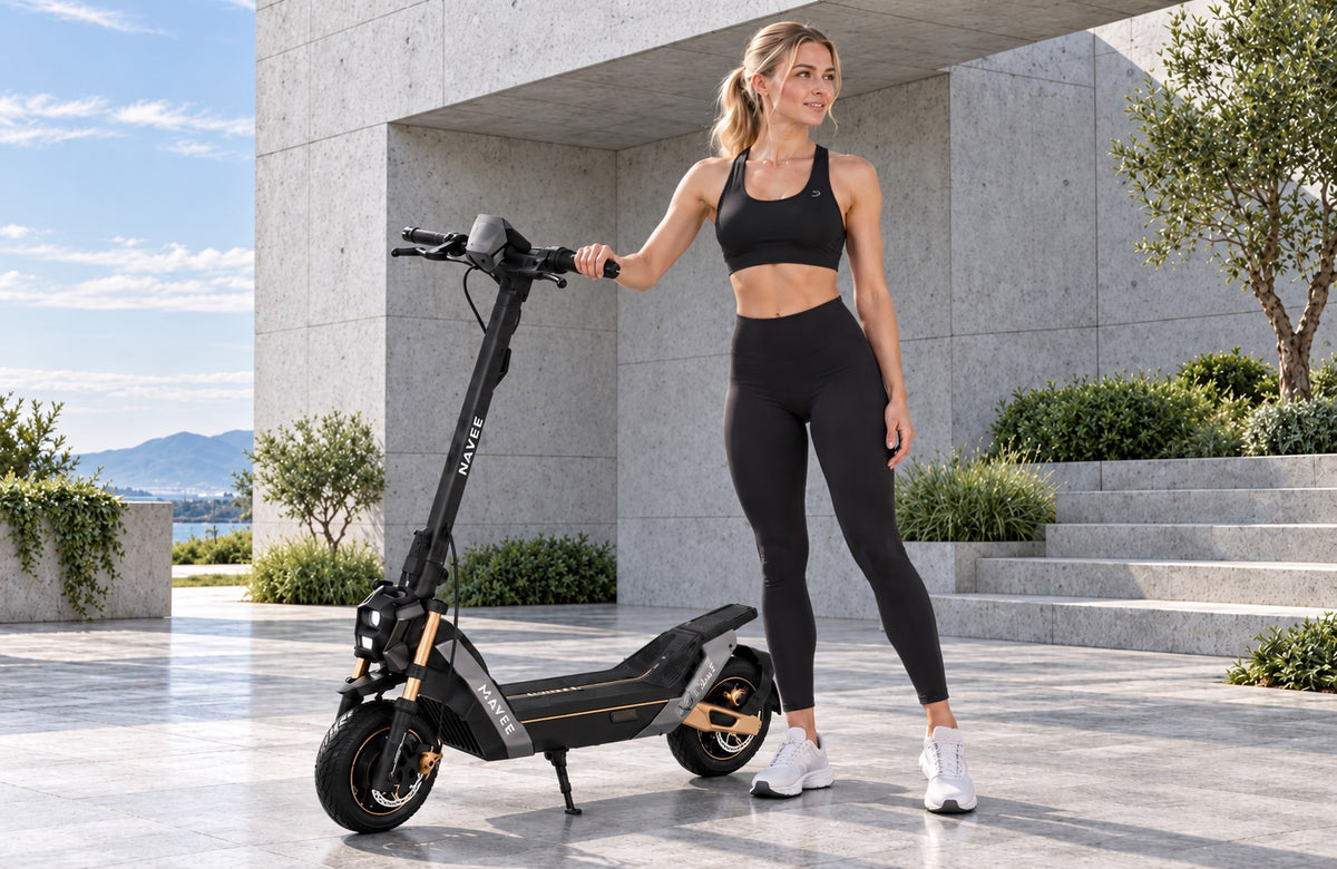 Mujer con un patinete eléctrico NAVEE frente a un edificio moderno de hormigón – sin motor de combustión, sin gases de escape, propulsado por electricidad