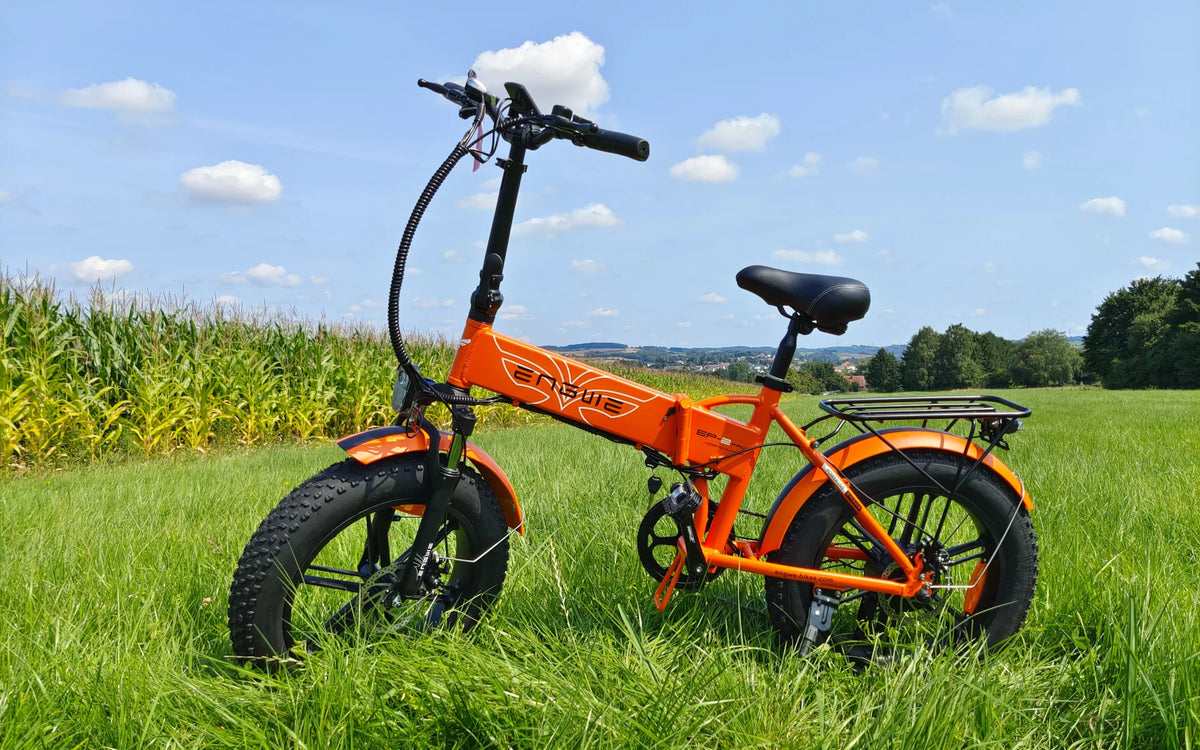 Bicicleta eléctrica plegable ENGWE EP-2 Pro naranja con ruedas anchas y portaequipajes en la hierba junto a un maizal