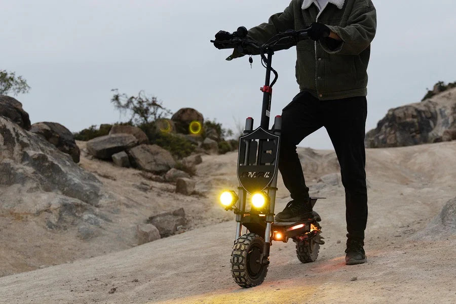 Patinete eléctrico con las luces delanteras encendidas al anochecer en un sendero rocoso