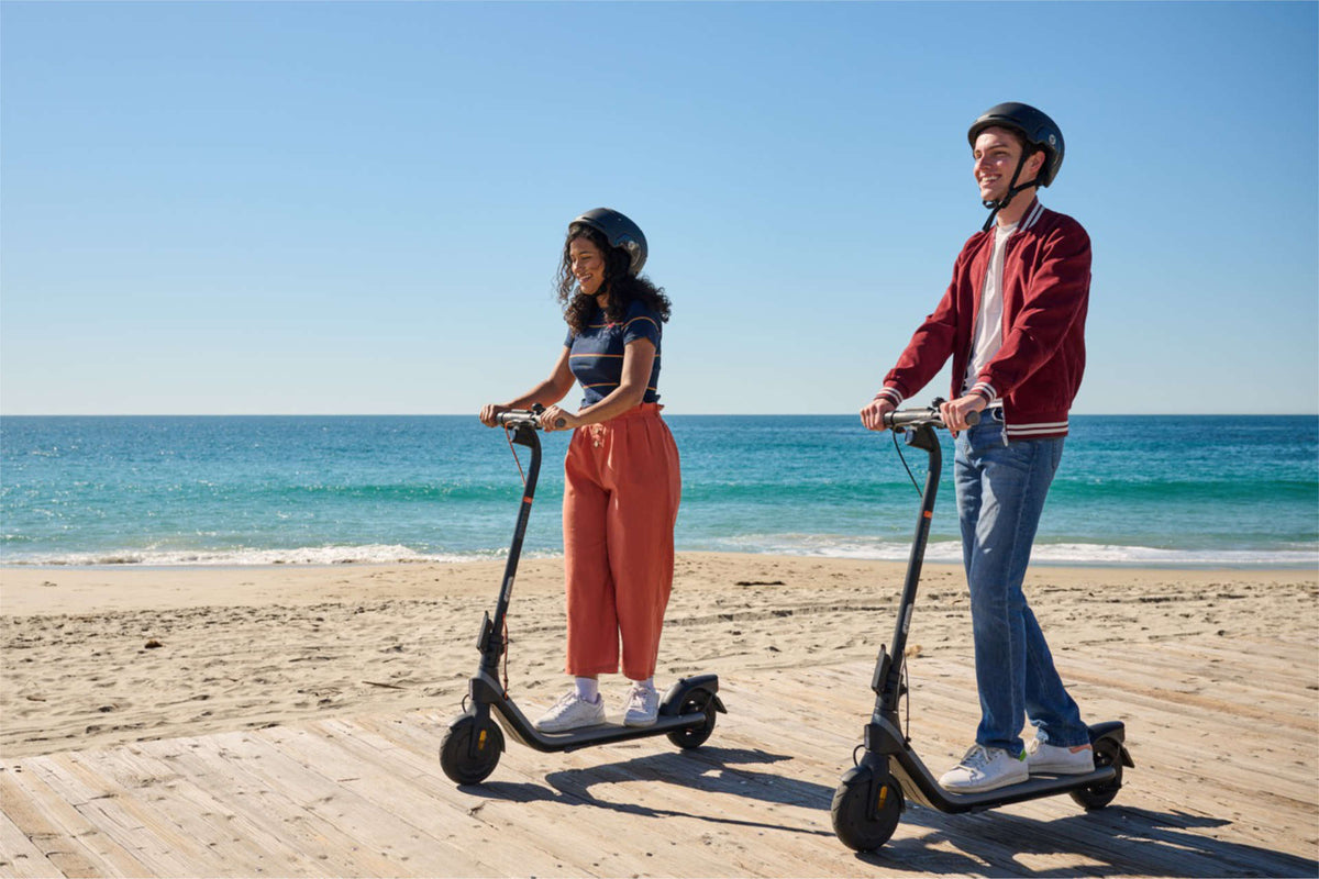 Dos personas con casco, cada una en su patinete eléctrico junto al mar – normativa del patinete eléctrico en España