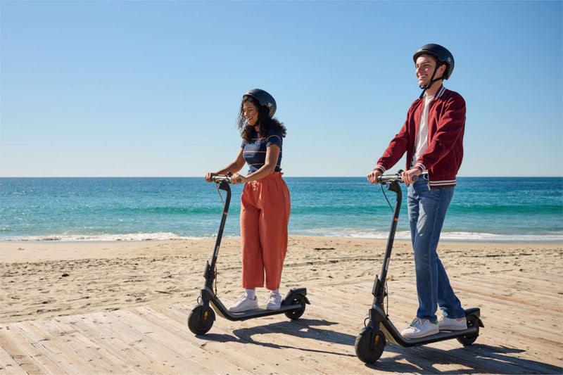 Dos personas con casco, cada una en su patinete eléctrico junto al mar – normativa del patinete eléctrico en España