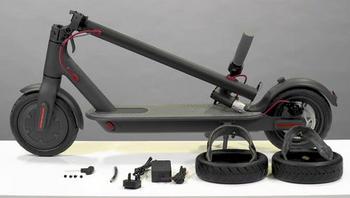 Patinete eléctrico plegado con recambios delante: dos neumáticos, un cargador y piezas pequeñas
