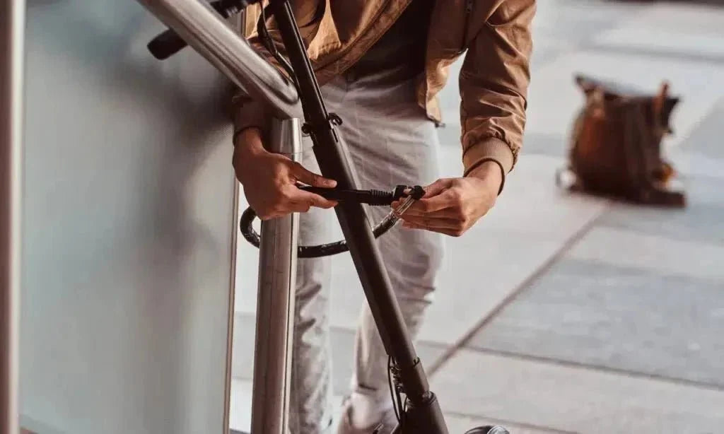 Una persona ata un patinete eléctrico a una barandilla con un candado de cable fino – cómo protegerlo del robo