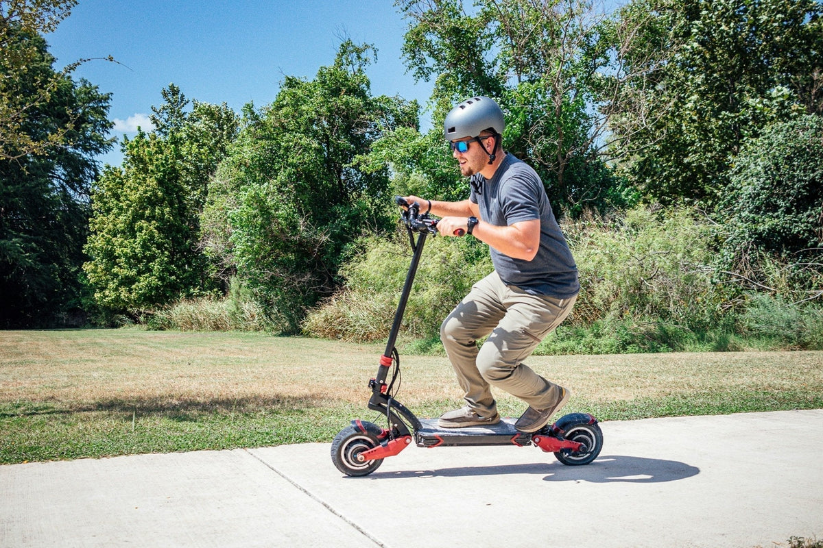 Hombre con casco en un patinete eléctrico por un camino asfaltado de un parque