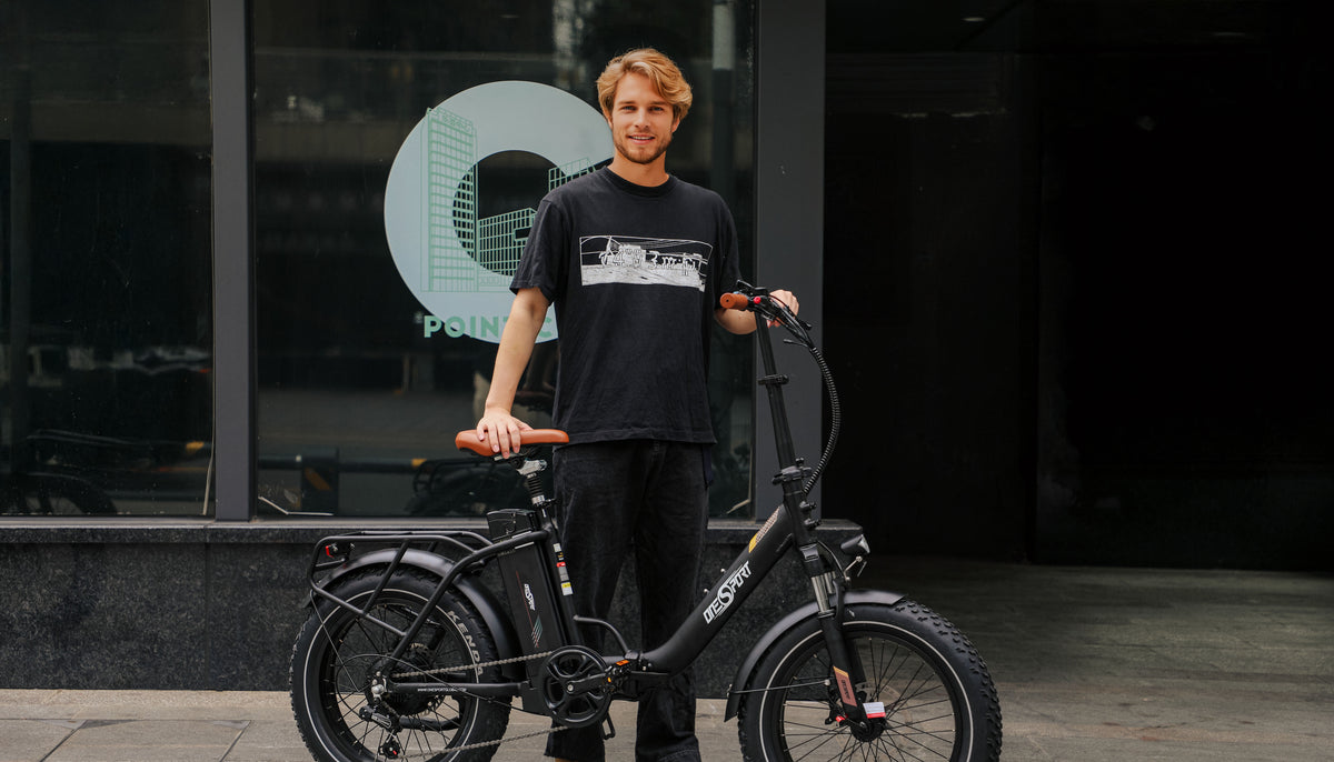 Hombre de pie junto a la bicicleta eléctrica plegable fat bike OneSport OT16 Max en color negro sobre fondo oscuro