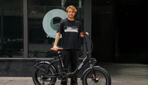 Hombre de pie junto a la bicicleta eléctrica plegable fat bike OneSport OT16 Max en color negro sobre fondo oscuro