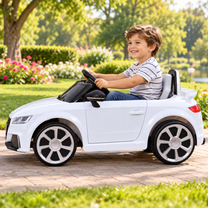 Niño conduciendo el coche eléctrico para niños Audi TT RS en color blanco en un parque