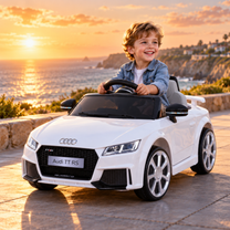 Niño conduciendo el coche eléctrico para niños Audi TT RS en color blanco junto al mar al atardecer