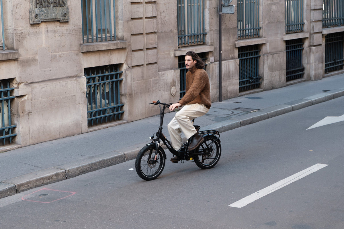 Hombre montando en bicicleta la OneSport OT16 Pro, bicicleta negra, por una calle junto a un edificio de piedra con rejas en las ventanas