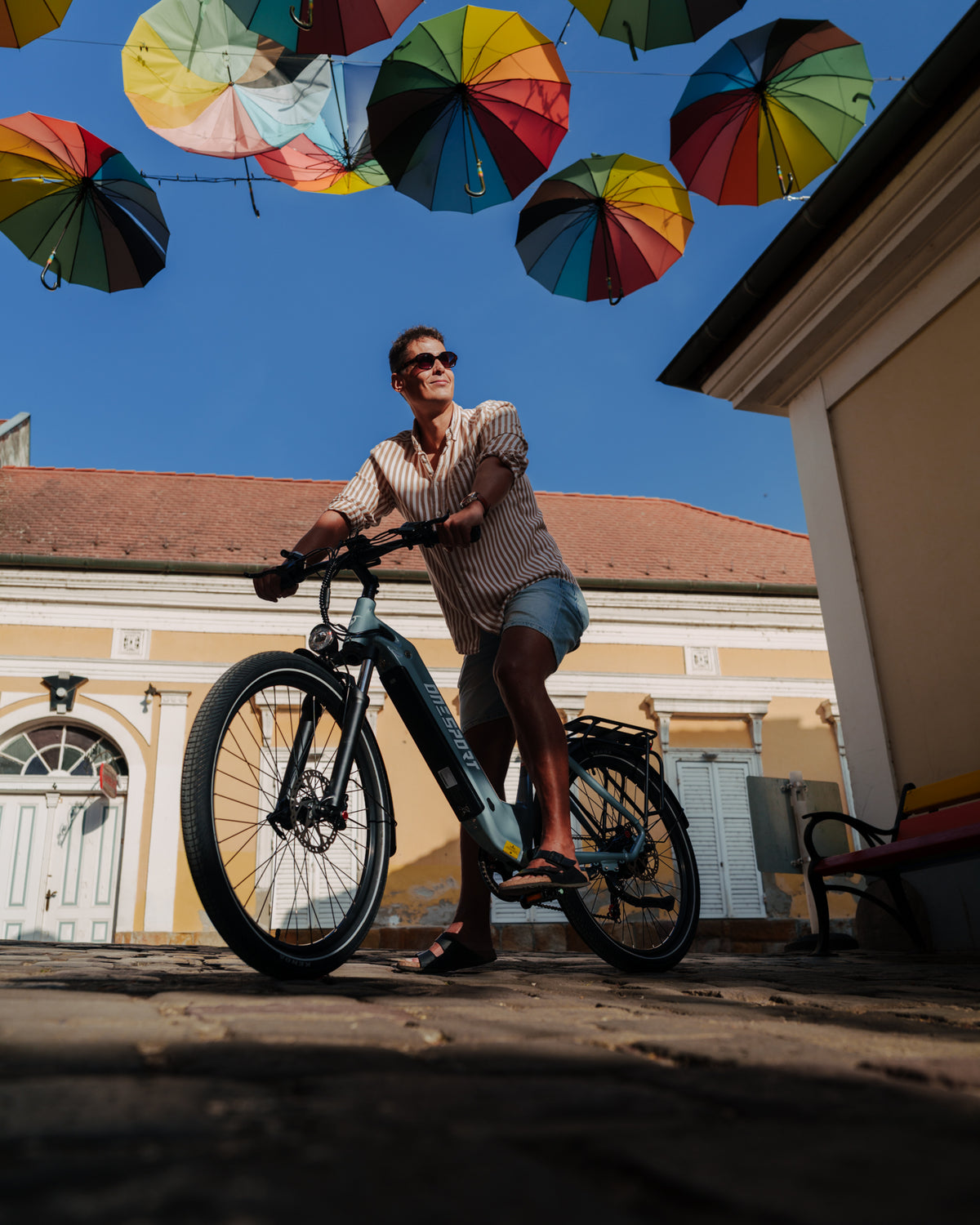 OneSport WT05 con un hombre de pie junto a la bicicleta en una calle empedrada bajo paraguas de colores