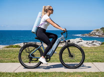 OneSport WT05 de perfil, mujer con una esterilla de yoga a la espalda pedalea junto al mar
