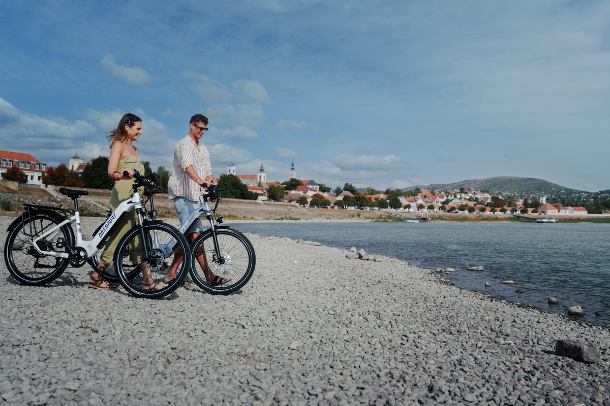 Dos personas caminan junto a sus OneSport WT05 por una orilla de piedra con ciudad y colina al fondo