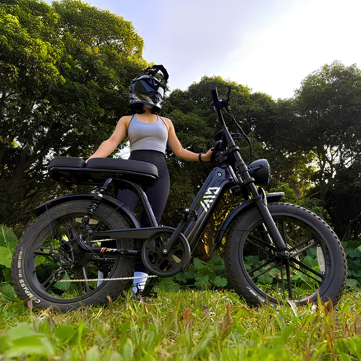 Mujer montando la bicicleta eléctrica fat bike TST R7 en color negro sobre el césped