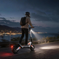 Persona con casco y mochila conduciendo el Wheely - J18 por una carretera costera al atardecer con el faro encendido