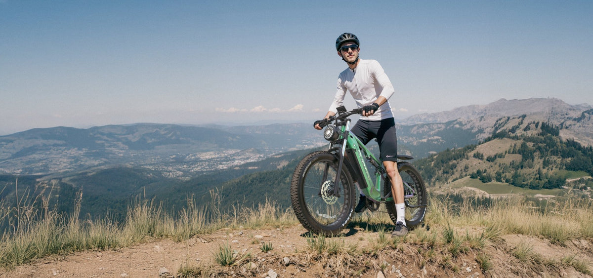 Hombre de pie junto a la bicicleta eléctrica fat bike Duotts E26 sobre el césped en la montaña