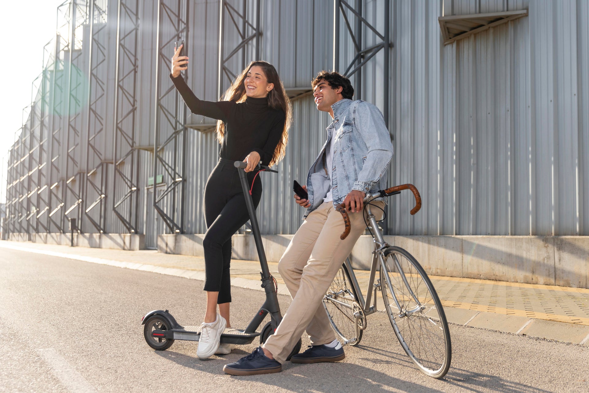 Una mujer en patinete eléctrico y un hombre en bicicleta al aire libre, a la luz del sol.