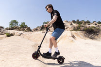 Persona circulando con el patinete eléctrico iScooter W6 por la ciudad sobre terreno arenoso