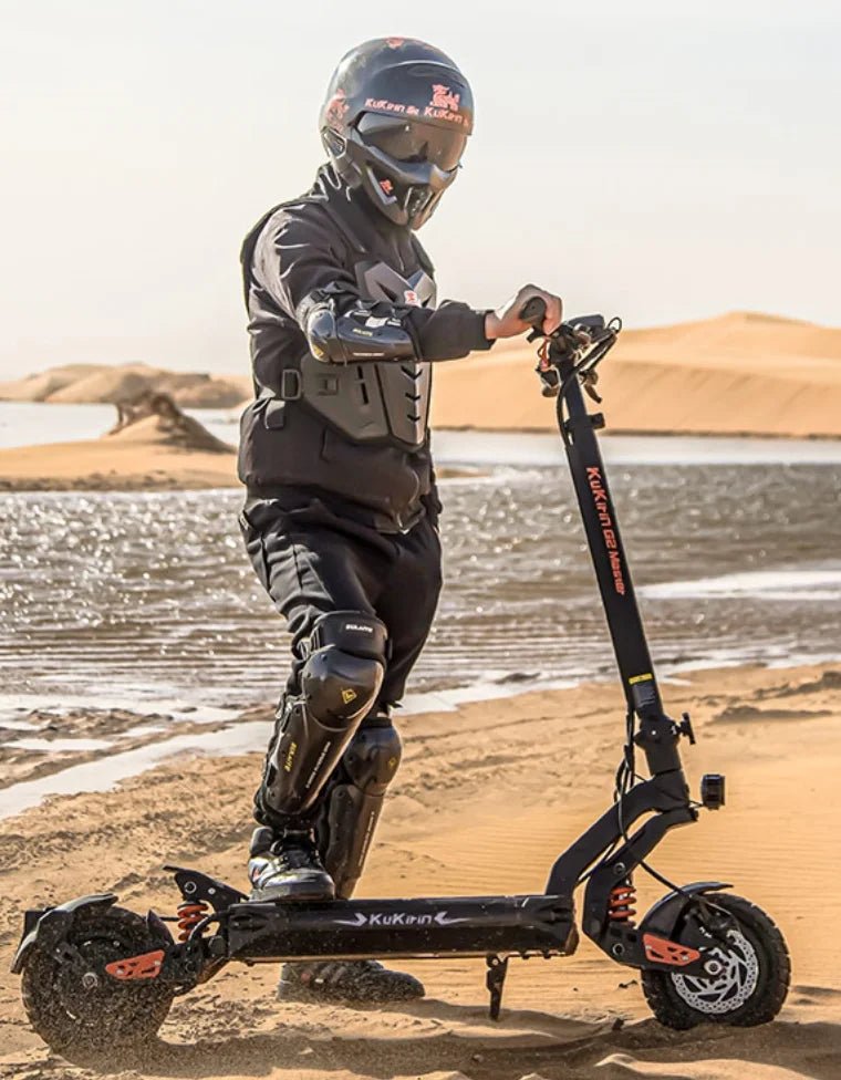 Persona de pie junto al patinete eléctrico KuKirin G2 Master con casco sobre terreno arenoso
