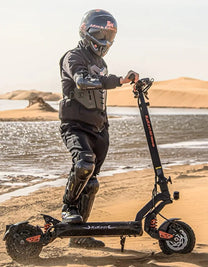 Persona de pie junto al patinete eléctrico KuKirin G2 Master con casco sobre terreno arenoso