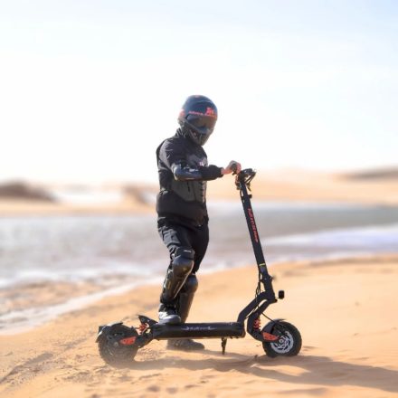 Persona de pie junto al patinete eléctrico KuKirin G2 Master sobre terreno arenoso