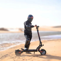 Persona de pie junto al patinete eléctrico KuKirin G2 Master sobre terreno arenoso