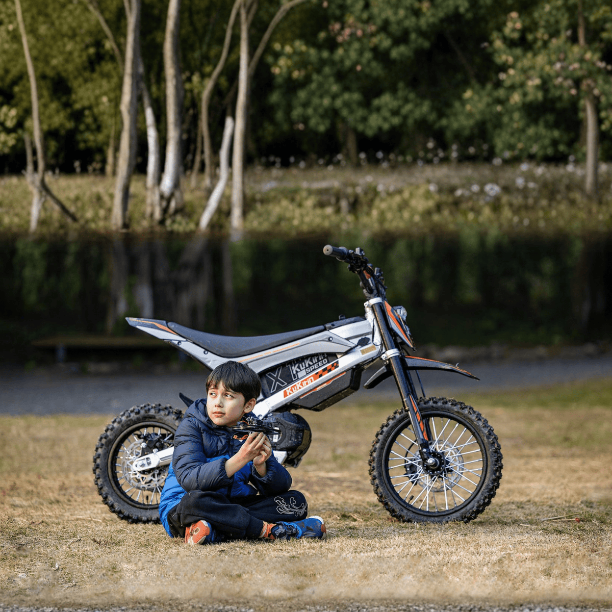 Persona sentada junto a la moto cross eléctrica KuKirin X1 con un niño