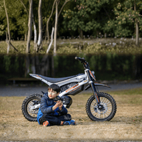 Persona sentada junto a la moto cross eléctrica KuKirin X1 con un niño