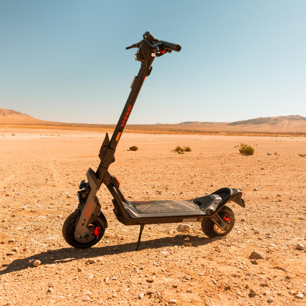 Persona de pie junto al patinete eléctrico Segway Ninebot GT3 sobre terreno arenoso