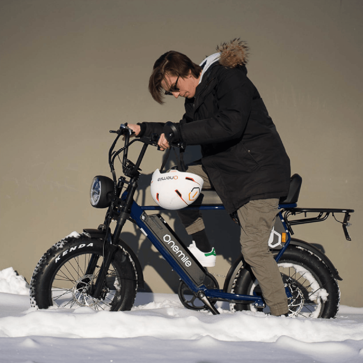 Hombre de pie junto a la bicicleta eléctrica fat bike Onemile P40 Pro con casco en un paisaje invernal
