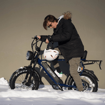 Hombre de pie junto a la bicicleta eléctrica fat bike Onemile P40 Pro con casco en un paisaje invernal
