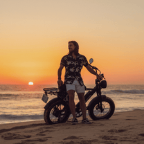 Hombre de pie junto a la bicicleta eléctrica fat bike Onemile P40 Pro junto al mar al atardecer
