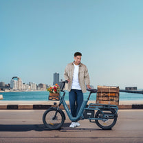 Hombre de pie junto a la bicicleta eléctrica OneSport OT01 junto al mar