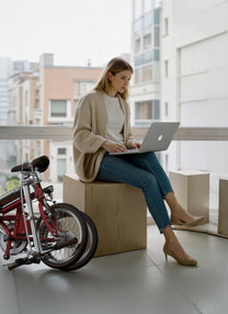 Persona sentada junto a la bicicleta eléctrica plegable OneSport OT02 en la ciudad