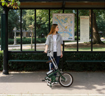 Mujer de pie junto a la bicicleta eléctrica plegable OneSport OT02 en la ciudad