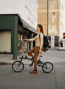 Mujer de pie junto a la bicicleta eléctrica plegable OneSport OT02 durante el plegado por una calle