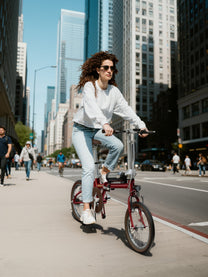 Mujer montando la bicicleta eléctrica plegable OneSport OT02 por la ciudad