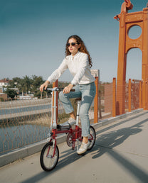 Mujer montando la bicicleta eléctrica plegable OneSport OT02 sobre un puente bajo el sol