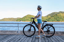 Mujer de pie junto a la bicicleta eléctrica OneSport OT12 en color negro junto al mar