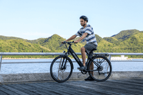 Hombre sentado en la bicicleta eléctrica OneSport OT12 en color negro junto al mar
