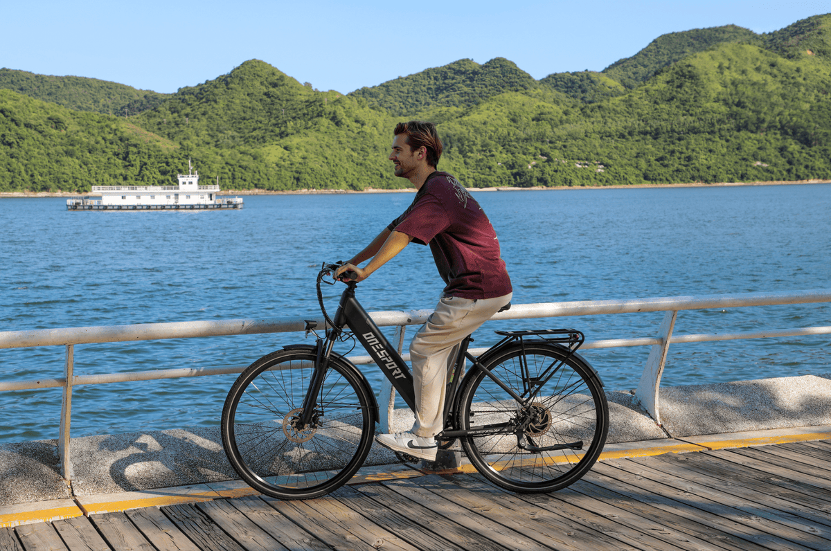 Persona montando la bicicleta eléctrica OneSport OT12 en color negro junto al mar
