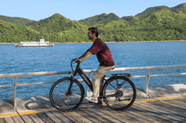 Persona montando la bicicleta eléctrica OneSport OT12 en color negro junto al mar
