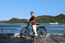 Hombre de pie junto a la bicicleta eléctrica OneSport OT12 en color negro junto al mar