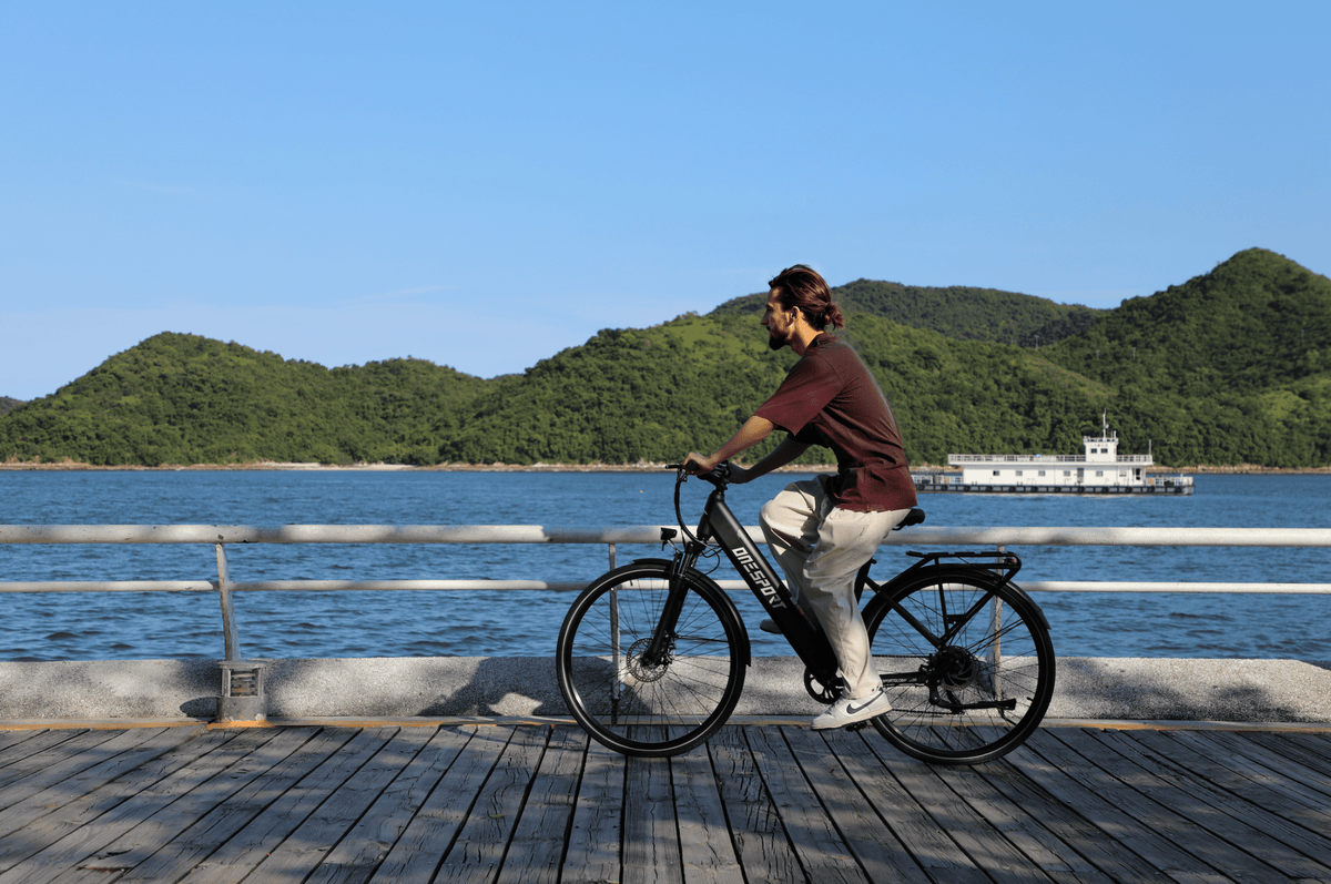 Hombre montando la bicicleta eléctrica OneSport OT12 en color negro junto al mar
