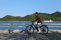 Hombre montando la bicicleta eléctrica OneSport OT12 en color negro junto al mar