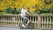 Hombre montando la bicicleta eléctrica plegable OneSport OT16-2 en color beige en un parque