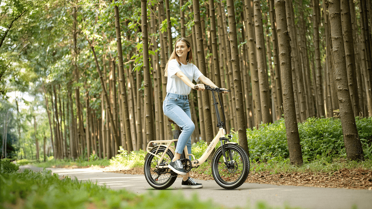 Mujer montando la bicicleta eléctrica plegable OneSport OT16-2 en color beige en el bosque