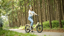 Mujer montando la bicicleta eléctrica plegable OneSport OT16-2 en color beige en el bosque