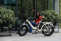 Mujer sentada en la bicicleta eléctrica plegable fat bike OneSport OT16 Max en color beige por una calle