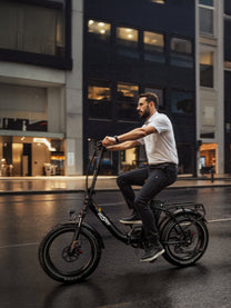 Hombre montando la bicicleta eléctrica plegable fat bike OneSport OT16 Max en color negro en un ambiente nocturno
